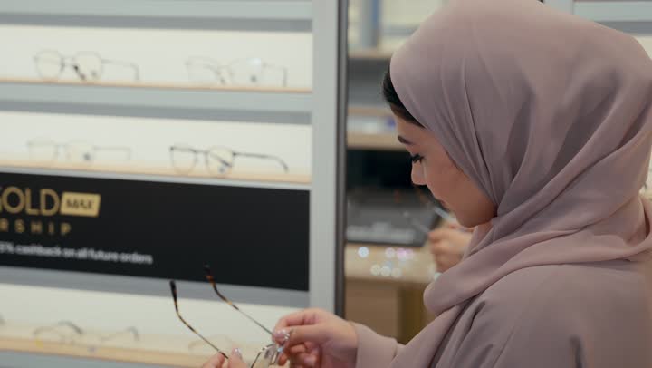 تجربة التسوق و اختيار النظارات الطبية ، امراتان عربيتان خليجيتان اماراتيان ترتديان العباءة و الحجاب تتبادلان الحديث و مشاركه الرأي داخل محل النظارات