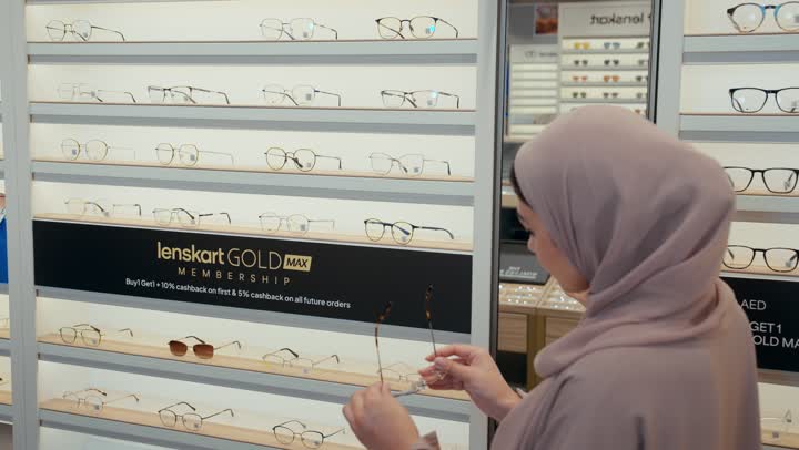 Choosing eyeglasses, a veiled Emirati Gulf Arab woman wearing a colorful abaya shopping inside an optical store, a Saudi woman comparing different frame shapes in front of a display window, the concept of eye care and modern shopping