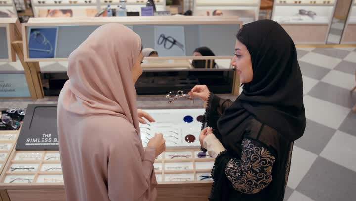 Sunglasses exhibition, a Gulf saleswoman displays a collection of glasses for an Emirati girl in an eyeglasses shop, purchasing sun protection glasses, a selection of elegant sunglasses, an Arab Gulf Emirati woman wearing a black abaya choosing the appropriate look