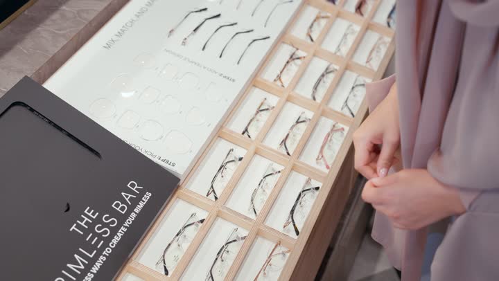 A wide new selection of eyeglasses in a Gulf store, glasses hidden in drawers for distinguished Emirati customers, a close-up of an Arab Gulf Emirati woman wearing a colorful abaya choosing eyeglasses, enjoying shopping in the mall