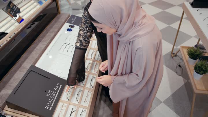 بائعة خليجية تعرض مجموعة من النظارات لفتاة اماراتية في محل نظارات , معرض نظارات شمسية، اقتناء نظارات حماية من الشمس, تشكيلة نظارات شمسية أنيقة ،  امراةعربية خليجيه اماراتية ترتدي العباءه السوداء تقوم باختيار الشكل المناسب