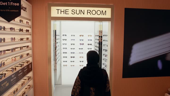 How to choose sunglasses that suit your facial features, a selection of elegant sunglasses, buying sun protection glasses, a photo from behind of an Emirati Gulf Arab woman wearing a black abaya entering a store to choose the appropriate look