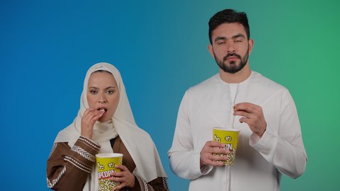 تناول الفوشار والمشروبات الباردة اثناء متابعة الأفلام والمسلسلات، قضاء وقت ممتع في السينما، تصوير مقرب لزوجيين عربيين خليجيين اماراتيين مبتسميين ينظران الى الكاميرا بتعابير السرور والسعادة والاندماج ، الاستمتاع بالأنشطة العائلية الترفيهيه، خلفية ملونه