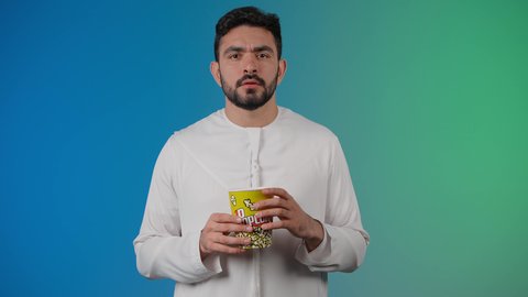 جهل امر ما ، قضاء أوقات ممتعة ومسلية، إيماءات وجه ويدين تدل على النسيان ،مفهوم التسليه والترفيه، رجل عربي خليجي اماراتي يرتدي الزى التقليدي يحمل بيده علبة الفشار ويقوم بمشاهده الافلام ، مشاهدة فيلم سينمائي