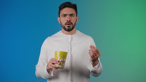 قضاء أوقات ممتعة ومسلية، إيماءات وجه ويدين تدل على الغضب ،مفهوم التسليه والترفيه، رجل عربي خليجي اماراتي يرتدي الزى التقليدي يحمل بيده علبة الفشار ويقوم بمشاهده الافلام ، مشاهدة فيلم سينمائي