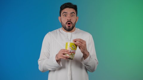 النظر بتعابير المفاجأه ، إيماءات وجه ويدين تدل على الصدمه والذهول ،مفهوم التسليه والترفيه، قضاء أوقات ممتعة ومسلية، رجل عربي خليجي اماراتي يرتدي الزى التقليدي يحمل بيده علبة الفشار ويقوم بمشاهده الافلام ، مشاهدة فيلم سينمائي