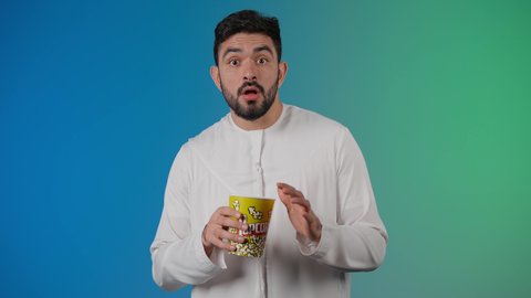 إيماءات وجه ويدين تدل على الصدمه والذهول ،مفهوم التسليه والترفيه، قضاء أوقات ممتعة ومسلية، رجل عربي خليجي اماراتي يرتدي الزى التقليدي يحمل بيده علبة الفشار ويقوم بمشاهده الافلام ، مشاهدة فيلم سينمائي