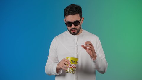 مفهوم التسليه والترفيه، قضاء أوقات ممتعة ومسلية، رجل عربي خليجي اماراتي يرتدي الزى التقليدي يحمل بيده علبة الفشار ويقوم بمشاهده الافلام ، إيماءات وجه ويدين تدل على السعادة والمتعة، مشاهدة فيلم سينمائي