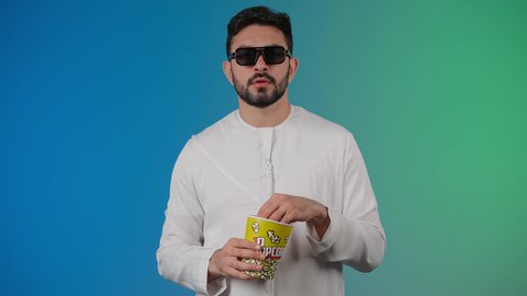 تعابير الخوف والرعب ، مفهوم التسليه والترفيه، قضاء أوقات ممتعة ومسلية، رجل عربي خليجي اماراتي يرتدي الزى التقليدي يحمل بيده علبة الفشار ويقوم بمشاهده الافلام ، إيماءات وجه ويدين تدل على السعادة والمتعة، مشاهدة فيلم سينمائي