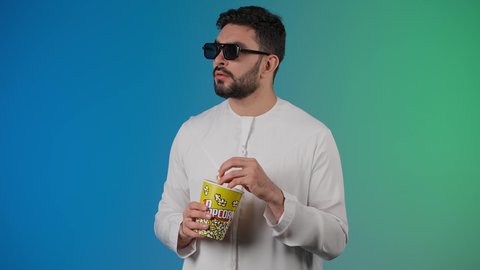 مفهوم التسليه والترفيه، قضاء أوقات ممتعة ومسلية، رجل عربي خليجي اماراتي يرتدي الكندوره والغتره يحمل بيده علبة الفشار ويقوم بمشاهده الافلام ، إيماءات وجه ويدين تدل على السعادة والمتعة، مشاهدة فيلم سينمائي