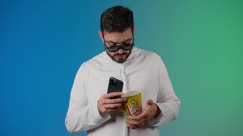 الدردشه عبر الانترنت ، دمج التقنيات الحديثه فى الحياه اليوميه ، قضاء أوقات ممتعة ومسلية، رجل عربي خليجي اماراتي يرتدي الكندوره والغتره يحمل بيده علبة الفشار ويعرض شاشه سوداء ، إيماءات وجه ويدين تدل على السعادة والمتعة، مشاهدة فيلم سينمائي، مفهوم التسليه والترفيه