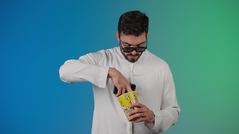 دمج التقنيات الحديثه فى الحياه اليوميه ، اجراء مكالمه هاتفيه عبر الجوال ، قضاء أوقات ممتعة ومسلية، رجل عربي خليجي اماراتي يرتدي الكندوره والغتره يحمل بيده علبة الفشار ويعرض شاشه سوداء ، إيماءات وجه ويدين تدل على السعادة والمتعة، مشاهدة فيلم سينمائي، مفهوم التسليه والترفيه