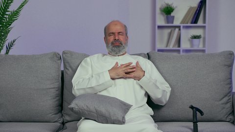 آلام الذبحة الصدرية، التعرض لنوبات قلبية مفاجئة، بورتريه لرجل عربي خليجي اماراتي يرتدي الكندوره يضع يده على قلبه بإيماءات الاحساس بوخز في الصدر والقلب، ايماءه التعب الشديد