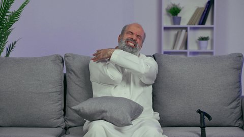 الحاجه لوضع خطة علاجية, إيماءات الألم في الأكتاف، التهاب العضلات والمفاصل، الإحساس بالتعب والإرهاق, رجل مسن عربي اماراتي خليجي يرتدي الكندورة يضع يده على رقبته بتعابير الوجع، طلب المساعده للذهاب الى الطبيب