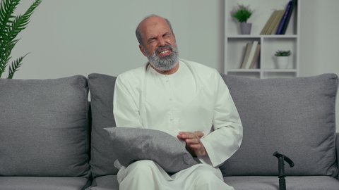 Introversion due to severe pain and fatigue, the need to rest and take appropriate treatment, feeling sick and having stomach pain, an elderly Arab Gulf Emirati man wearing a kandura, putting his hands on his stomach with an expression of pain, colon pain