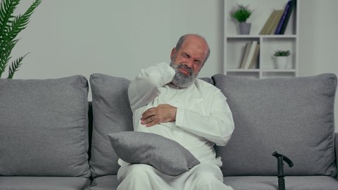 الحاجه لوضع خطة علاجية, إيماءات الألم في الأكتاف، التهاب العضلات والمفاصل، الإحساس بالتعب والإرهاق, رجل مسن عربي اماراتي خليجي يرتدي الكندورة يضع يده على رقبته بتعابير الوجع، طلب المساعده للذهاب الى الطبيب