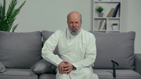 ايماءات الوجه تدل على الاضطراب والوجع، التهاب المفاصل والغضاريف وآلام العظام ، ضرورة الذهاب للطبيب والحصول على العلاج، رجل كبير السن عربي خليجي إماراتي يرتدي والكندورة يمسك ركبته بإيماءات التألم