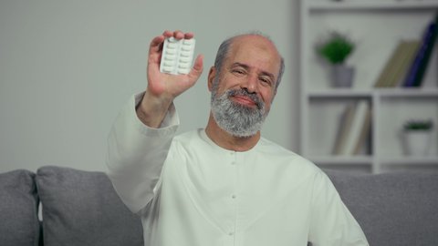 مريض عربي اماراتي خليجي كبير بالسن يقوم بتلقي العلاج في المستشفى, الاهتمام بالصحة والالتزام بالأوقات الصحيحة لأخذ العلاج, استخدام عقار الدواء بوصفة طبية, رجل كبير بالسن عربي خليجي اماراتي يرتدي الكندوره يجلس علي اريكه ويحمل شريط الدواء