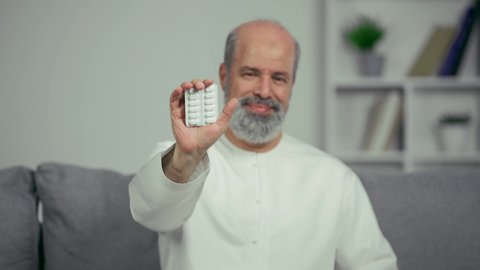 مريض عربي اماراتي خليجي كبير بالسن يقوم بتلقي العلاج في المستشفى, الاهتمام بالصحة والالتزام بالأوقات الصحيحة لأخذ العلاج, استخدام عقار الدواء بوصفة طبية, رجل كبير بالسن عربي خليجي اماراتي يرتدي الكندوره يجلس علي اريكه ويحمل شريط الدواء
