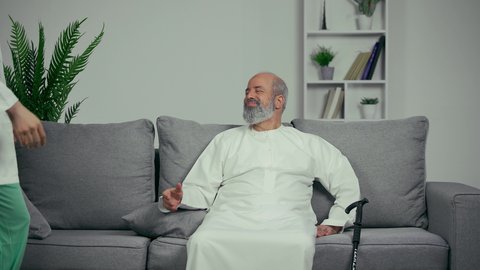 احترام كبار السن، طبيب اماراتي يصافح مريض مسن، رجل مسن يرتدي كندوره يجلس علي اريكه رماديه بجوار العكاز