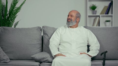 مفهوم المواساه واحترام كبار السن، طبيب اماراتي يصافح مريض مسن، رجل مسن يرتدي كندوره يجلس علي اريكه رماديه بجوار العكاز