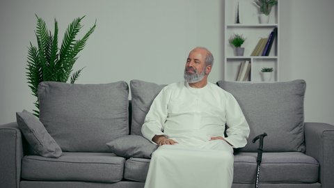 مفهوم المواساه واحترام كبار السن، طبيب اماراتي يصافح مريض مسن، رجل مسن يرتدي كندوره يجلس علي اريكه رماديه بجوار العكاز