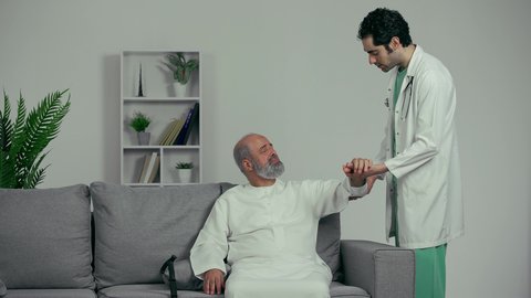 مريض عربي اماراتي كبير بالسن يشكو من آلام في الكتف واليد,  طبيب اماراتي يرتدي المعطف الابيض يقوم بفحص المريض والتأكد من سلامة اليد, صحة وأطباء, حالة مرضية, مهن ووظائف طبيه، ايماءه التعب الشديد