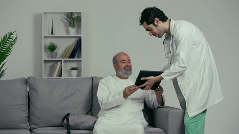 طبيب عربي خليجي اماراتي يقوم بطمأنة مريض كبير بالسن بالنتائج عن طريق التكنولوجيا المتطورة, رؤية التحاليل والنتائج عن طريق التابلت, مفهوم الرعاية الصحية عن بعد عن طريق التكنولوجيا المتطورة، دمج التكنولوجيا الحديثه بالطب