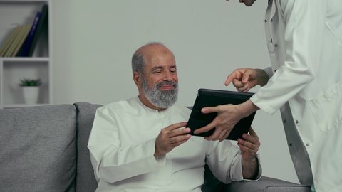 طبيب عربي خليجي اماراتي يقوم بطمأنة مريض كبير بالسن بالنتائج عن طريق التكنولوجيا المتطورة, رؤية التحاليل والنتائج عن طريق التابلت, مفهوم الرعاية الصحية عن بعد عن طريق التكنولوجيا المتطورة، دمج التكنولوجيا الحديثه بالطب