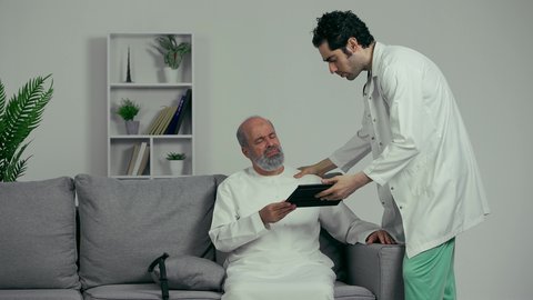 نتائج الفحوصات الغير مرضيه، طبيب عربي خليجي اماراتي يقوم بإستخدام جهاز التابلت لرؤية تحاليل ونتائج المرضى، مريض كبير في السن في زيارة إلى طبيب لفحص حالته الصحية، مفهوم الطب والرعاية الطبية، إستخدام ودمج التكنولوجيا بمجال الطب