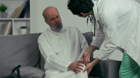 آلام العضلات والمفاصل, مفهوم الطب والرعاية الصحية, طبيب اماراتي  يقوم بفحص ركبة رجل مسن للتأكد من سلامتها من الكسر، رجل مسن يشتكي من ألم خشونه الركبه