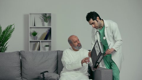 القيام بالفحوصات الطبية اللازمة , تقديم خدمات الرعاية الصحية , طبيب عربي خليجي اماراتي يرتدي المعطف وسماعه الفحص الطبيه يحمل دفتر سجلات المرضى بيده يقوم مراجهع الحاله الصحيه للمريض