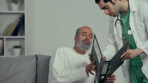 القيام بالفحوصات الطبية اللازمة , تقديم خدمات الرعاية الصحية , طبيب عربي خليجي اماراتي يرتدي المعطف وسماعه الفحص الطبيه يحمل دفتر سجلات المرضى بيده يقوم مراجهع الحاله الصحيه للمريض