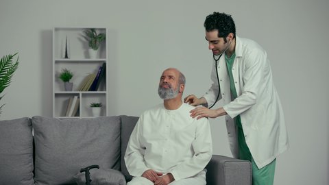 الشعور بالالم في الصدر والرئه، فحص نبضات القلب, ايماءات التنفس بعمق، طبيب اماراتي يرتدي المعطف الابيض يحمل سماعه الفحص الطبيه يقوم بفحص مريض مسن، الشعور بالتعب والارهاق