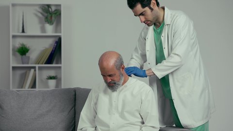 الحاجة للعلاج الفيزيائي، الإحساس بالتعب والإرهاق, وجع مفاصل و عظام الرقبة, آلام العنق والعمود الفقري, طبيب عربي خليجي إماراتي يرتدي المعطف الابيض والقفزات يقوم بفحص رجل مسن، رجل مسن يرتدي كندوره يعاني من آلام الفقرات