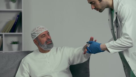 مفهوم الطب و الرعاية الصحية,  طبيب عربي خليجي اماراتي يرتدي المعطف الابيض والقفازات يقوم بقياس الضغط باستخدام جهاز الميزان الالكتروني لمريض مسن يرتدي طاقيه وكندوره بيضاء، استخدام الاجهزة الطبية الحديثة