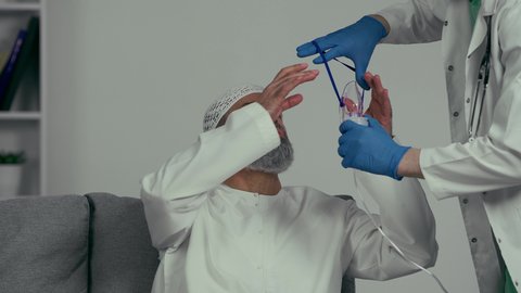 معالجة حالات ضيق التنفس، تأمين الراحة للعضلات التنفسية باستخدام جهاز التنفس الصناعي،  رجل عربي اماراتي خليجي يرتدي الكندوره والغتره يقوم بوضع قناع الرذاذ لاستنشاق الاكسجين، تقديم الخدمات الصحية، طبيب يقوم بوضع قناع التنفس للمريض المسن