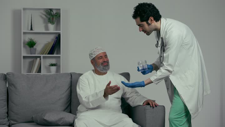 Medicine and healthcare, medications for treating medical conditions and preventing diseases, the concept of pharmacy and medical supplies, a close-up of an Arab Gulf Emirati doctor wearing a white coat holding a patient's medication dose in his hand, an elderly man taking medication