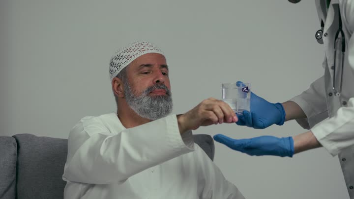 Medicine and healthcare, medications for treating medical conditions and preventing diseases, the concept of pharmacy and medical supplies, a close-up of an Arab Gulf Emirati doctor wearing a white coat holding a patient's medication dose in his hand, an elderly man taking medication