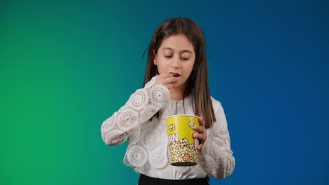 ايماءات الاستمتاع بمشاهدة فيلم ممتع، متابعة الأفلام والعروض المسرحية في السينما، الاشاره الى موقع معين ، الابتعاد عن روتين الحياة اليومية، تصوير لبنت عربية خليجية اماراتيه مبتسمة ترتدي الزي الكاجوال ونظاره سوداء تمسك بيدها علبه الفوشار ، خلفية ملونه