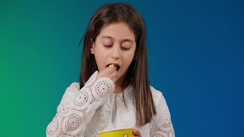 متابعة الأفلام والعروض المسرحية في السينما، الاشاره الى موقع معين ،ايماءات الاستمتاع بمشاهدة فيلم ممتع،الابتعاد عن روتين الحياة اليومية، تصوير لبنت عربية خليجية اماراتيه مبتسمة ترتدي الزي الكاجوال ونظاره سوداء تمسك بيدها علبه الفوشار ، خلفية ملونه