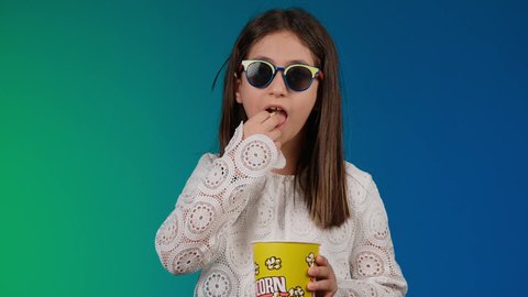 الاهتمام بالاناقه والمظهر الخارجي ،الابتعاد عن روتين الحياة اليومية، ايماءات الاستمتاع بمشاهدة فيلم ممتع، متابعة الأفلام والعروض المسرحية في السينما، تصوير لبنت عربية خليجية اماراتيه مبتسمة ترتدي الزي الكاجوال ونظاره سوداء تمسك بيدها علبه الفوشار ، خلفية ملونه