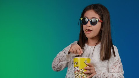 متابعة الأفلام والعروض المسرحية في السينما، تعابير النعاس والارهاق، الابتعاد عن روتين الحياة اليومية،  ايماءات الاستمتاع بمشاهدة فيلم ممتع، تصوير لبنت عربية خليجية اماراتيه مبتسمة ترتدي الزي الكاجوال ونظاره سوداء تمسك بيدها علبه الفوشار ، خلفية ملونه