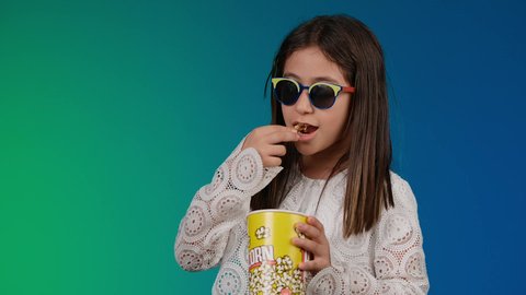 ايماءات النعاس والارهاق،  الابتعاد عن روتين الحياة اليومية،  متابعة الأفلام والعروض المسرحية في السينما، ايماءات الاستمتاع بمشاهدة فيلم ممتع، تصوير لبنت عربية خليجية اماراتيه مبتسمة ترتدي الزي الكاجوال ونظاره سوداء تمسك بيدها علبه الفوشار ، خلفية ملونه