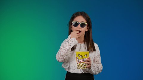 متابعة الأفلام والعروض المسرحية في السينما، ايماءات الاستمتاع بمشاهدة فيلم ممتع، تحديد هدف معين ، الاشاره باصبع السبابه الى شئ ما ، الابتعاد عن روتين الحياة اليومية، بورتريه لبنت عربية خليجية اماراتيه مبتسمة ترتدي الزي الكاجوال ونظاره سوداء تمسك بيدها علبه الفوشار ، خلفية ملونه