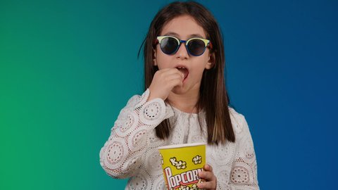 ايماءات الاستمتاع بمشاهدة فيلم ممتع، تحديد هدف معين ، الاشاره باصبع السبابه الى شئ ما ، متابعة الأفلام والعروض المسرحية في السينما، الابتعاد عن روتين الحياة اليومية، بورتريه لبنت عربية خليجية اماراتيه مبتسمة ترتدي الزي الكاجوال ونظاره سوداء تمسك بيدها علبه الفوشار ، خلفية ملونه