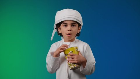 مفهوم الترفيه عن النفس والتسلية ,تصوير لولد عربي اماراتي خليجي يرتدي الكندورة والغتره يمسك بيده علبه الفوشار, متابعة الأفلام والعروض المسرحية في السينما، الابتعاد عن روتين الحياة اليومية