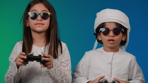 Gestures and hand movements indicating the challenge of the game, spending fun times playing electronic games, the concept of fun and entertainment, the concept of entertaining recreational activities with the family, a picture of an Arab Gulf Emirati boy holding a joystick in his hand playing with his sister, a family atmosphere full of happiness and love, a colorful background