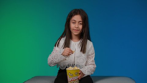 قضاء اوقات ممتعة باللعب ، استخدام التقنيات الحديثة للتسلية والترفيه، تصوير لبنت عربية خليجية اماراتيه مبتسمة ترتدي الزي الكاجوال تجلس على اريكة رمادية تقوم باللعب في ألعاب الفيديو بتعابير وايماءات الاندماج والتركيز، خلفية ملونه