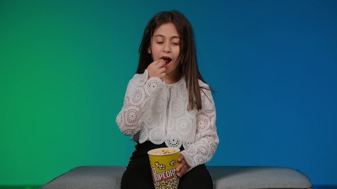 Expressions of confusion and ignorance, using modern technology for entertainment and amusement, having a good time playing, a picture of a smiling Emirati Gulf Arab girl wearing casual clothes sitting on a gray couch playing video games with expressions and gestures of integration and concentration, colorful background